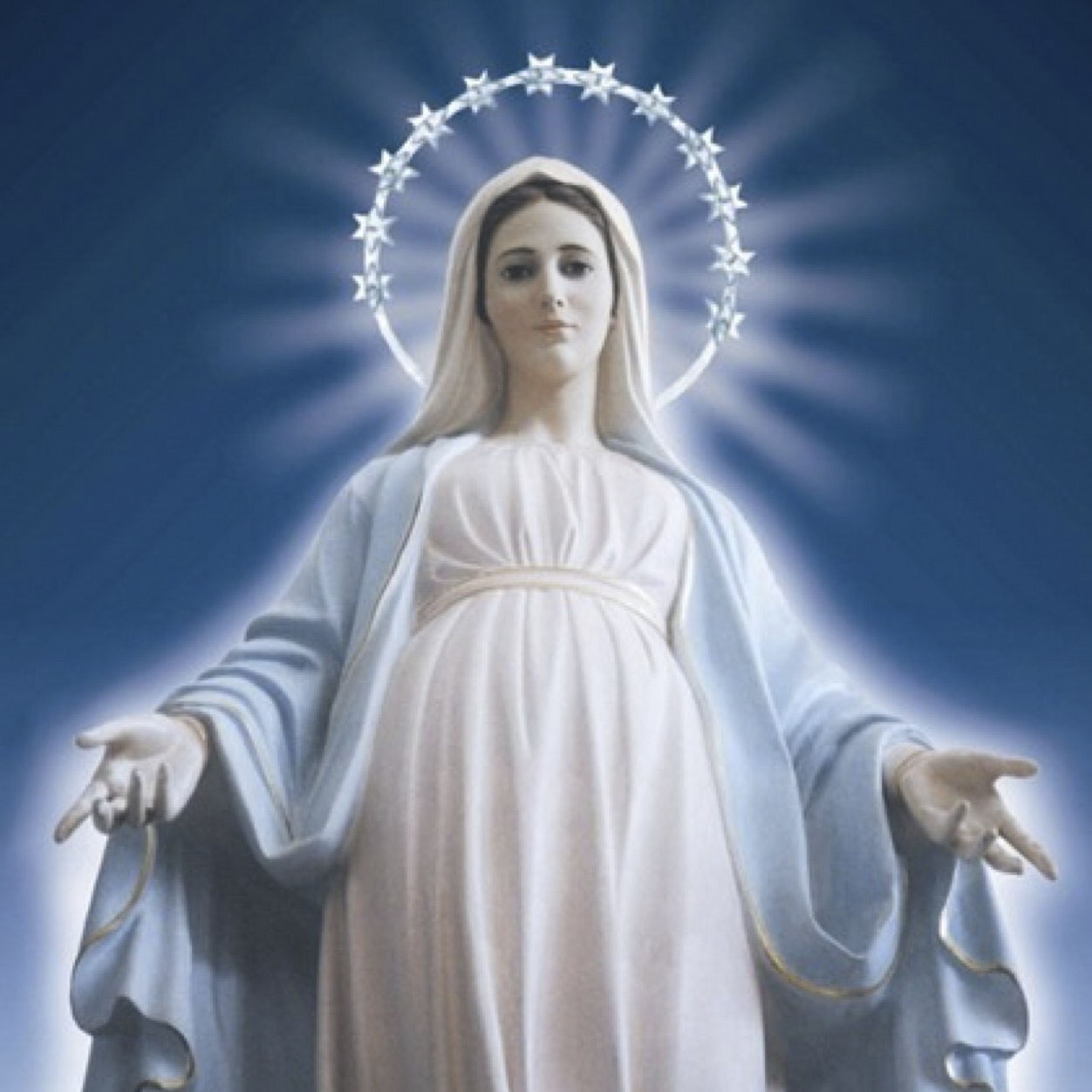 Statue of the Virgin Mary in white and pale blue robes, arms open, a ring of stars around her head, against a deep blue ground